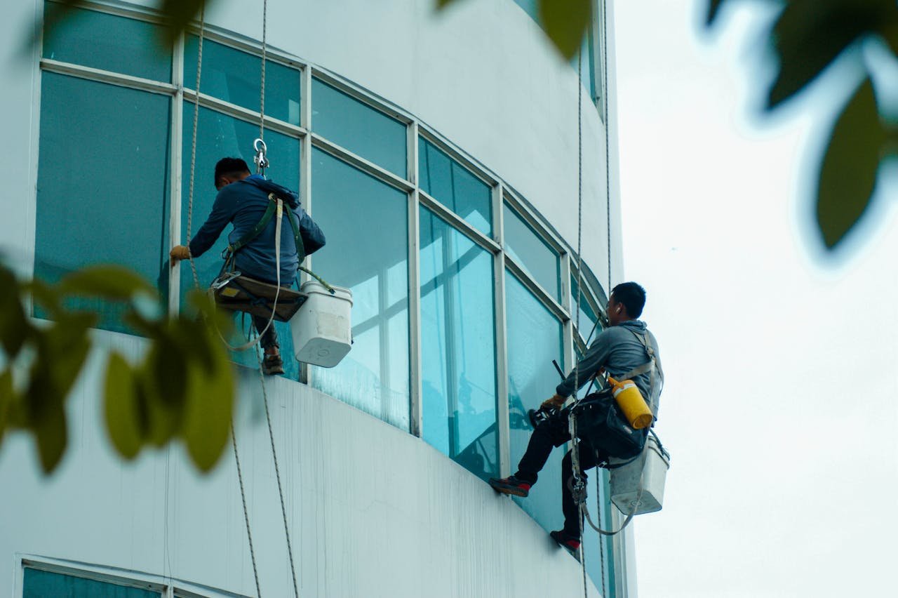 Window cleaners suspended on ropes clean a high-rise building's glass exterior.
